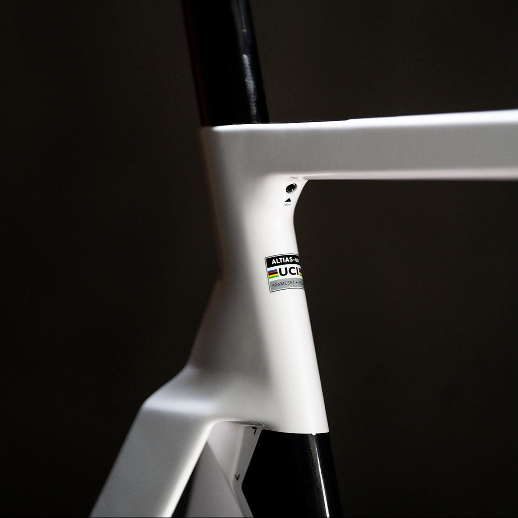 Close-up of a white and black bicycle frame with a black seat post, featuring a small UCI logo decal on the white down tube, set against a dark background.