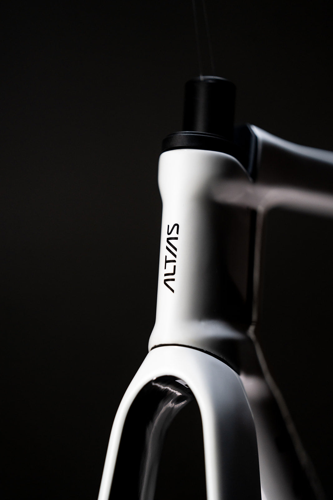 Close-up of a white and black road bicycle frame with the brand name 'ALTIAS' printed vertically on the white head tube, set against a dark black background.