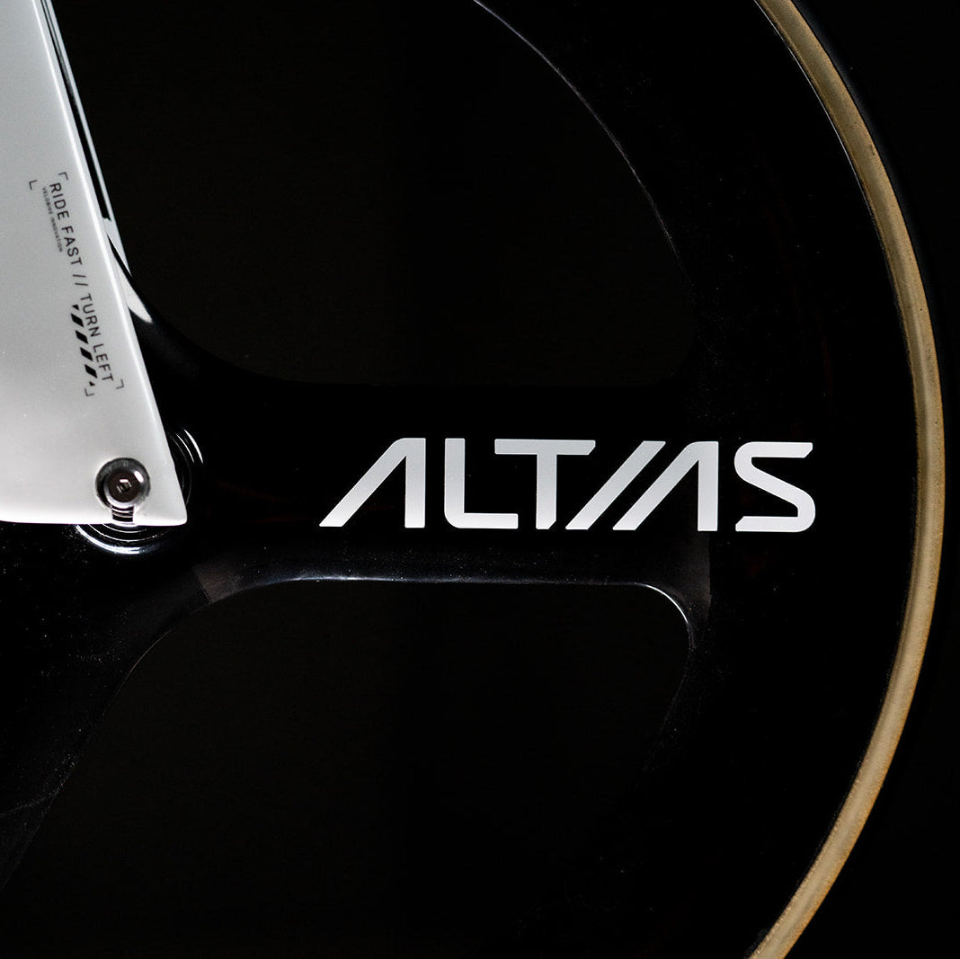 Close-up of a black bicycle wheel with in a bike fork and the white ALTIAS brand logo on the frame, set against a dark background.