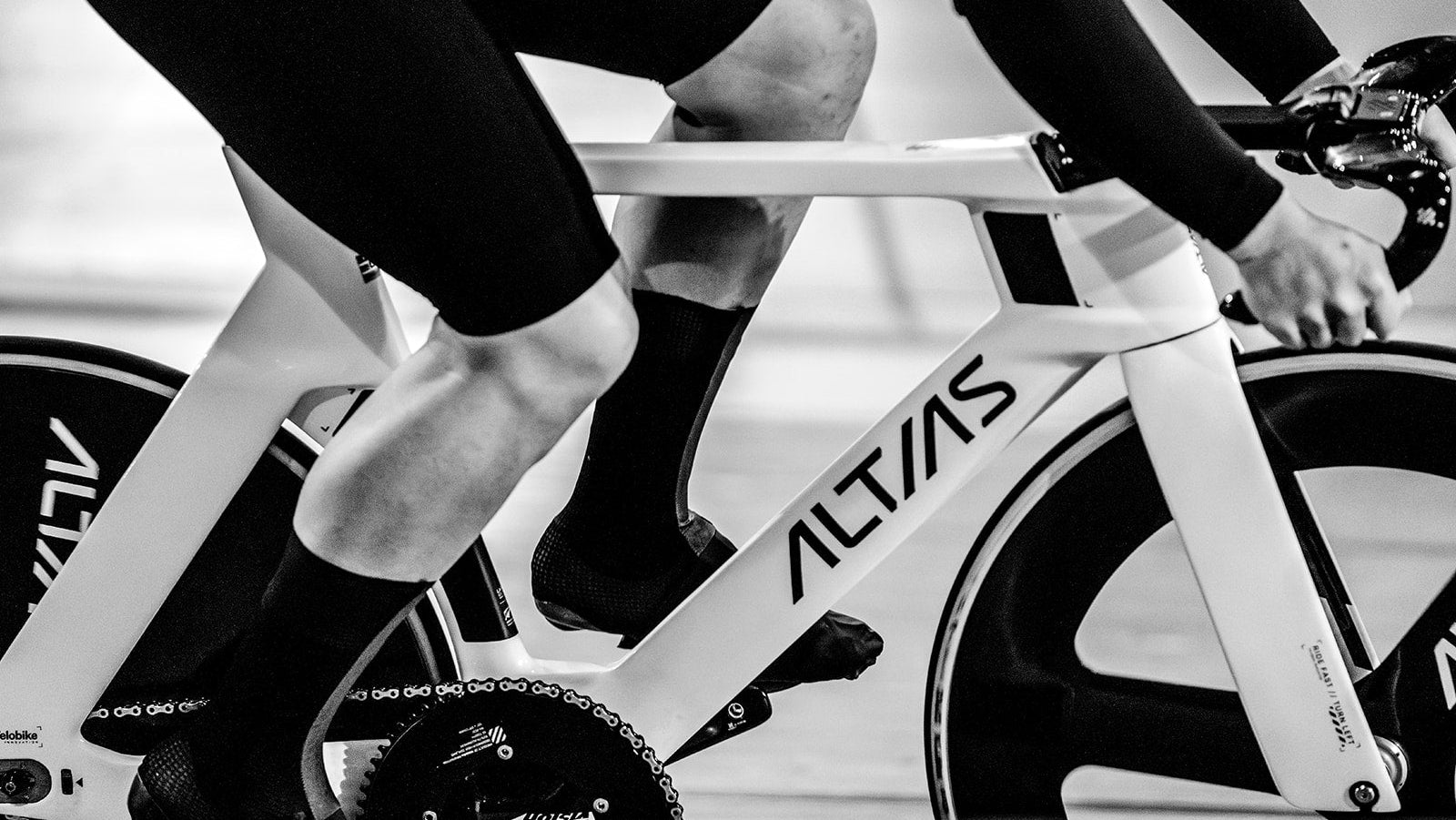 black and white photo of an athlete riding a white track bike on a wooden velodrome